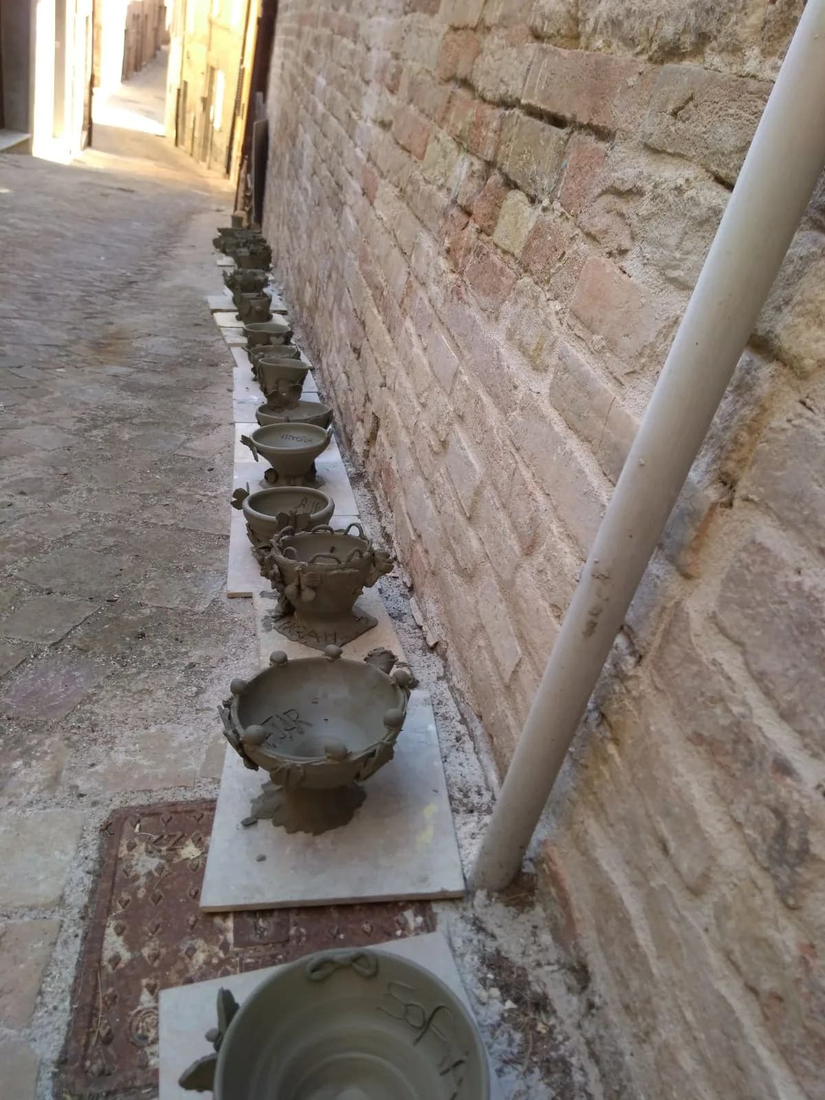 Una fila di ciotole appena tornite, ad asciugare lungo un muro di mattoni.