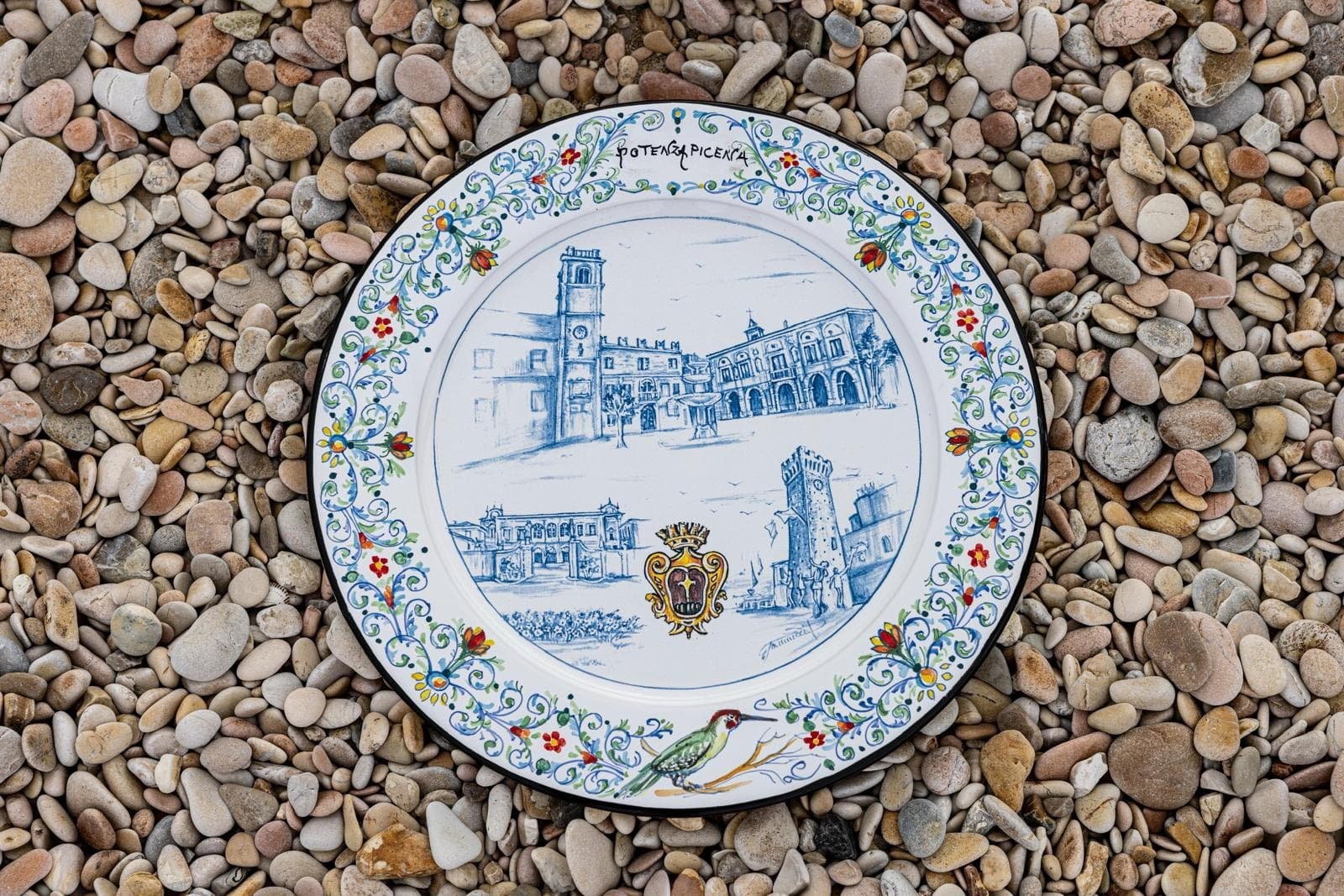 Maiolica plate dedicated to Porto San Giorgio resting on the dry pebbles of the beach.