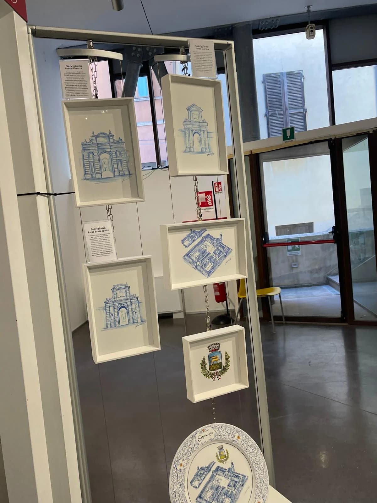 I disegni incorniciati dentro le nicchie bianche, lungo la parete della sala.