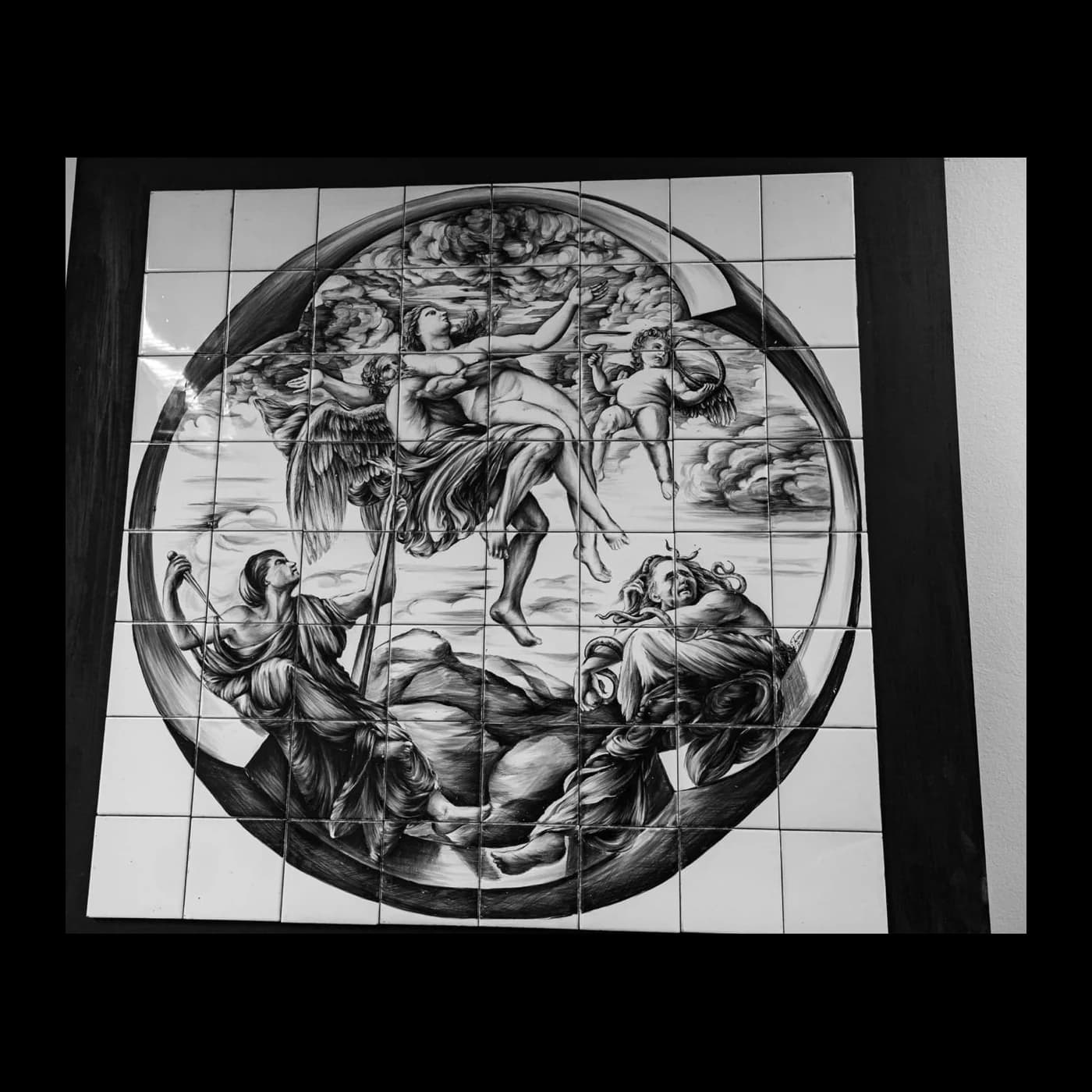 Composizione circolare dipinta in monocromo su un pannello quadrato di piastrelle, con figure disposte lungo il cerchio.