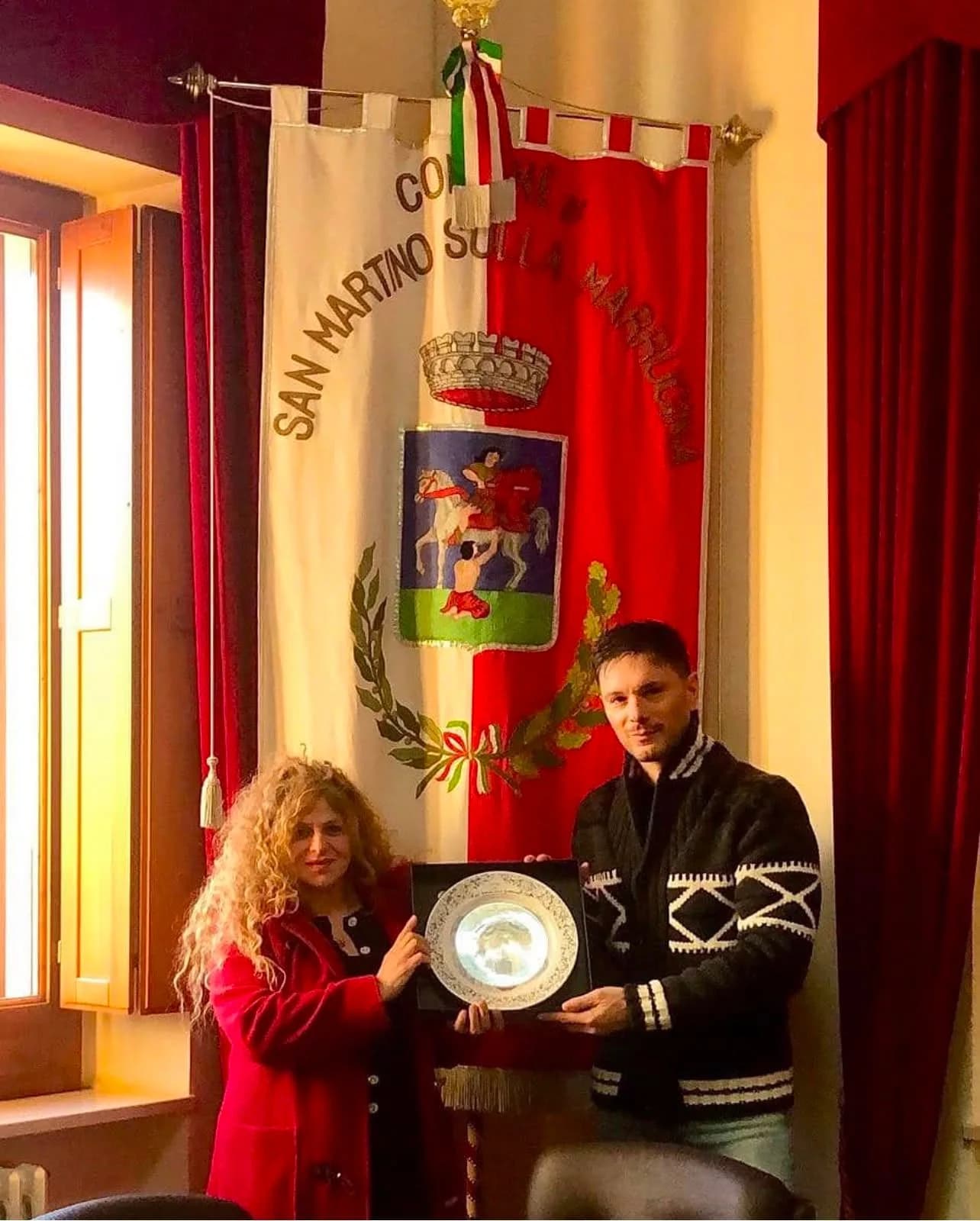 Davanti allo stendardo del Comune di San Martino sulla Marrucina, due persone reggono il piatto.