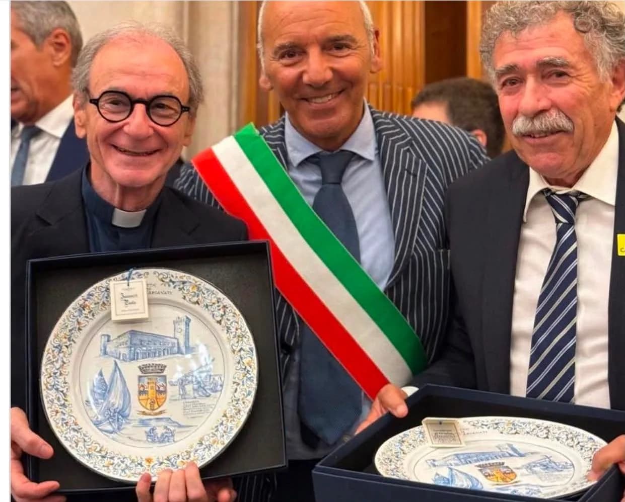 Tre persone con due piatti incorniciati, al termine di una cerimonia.