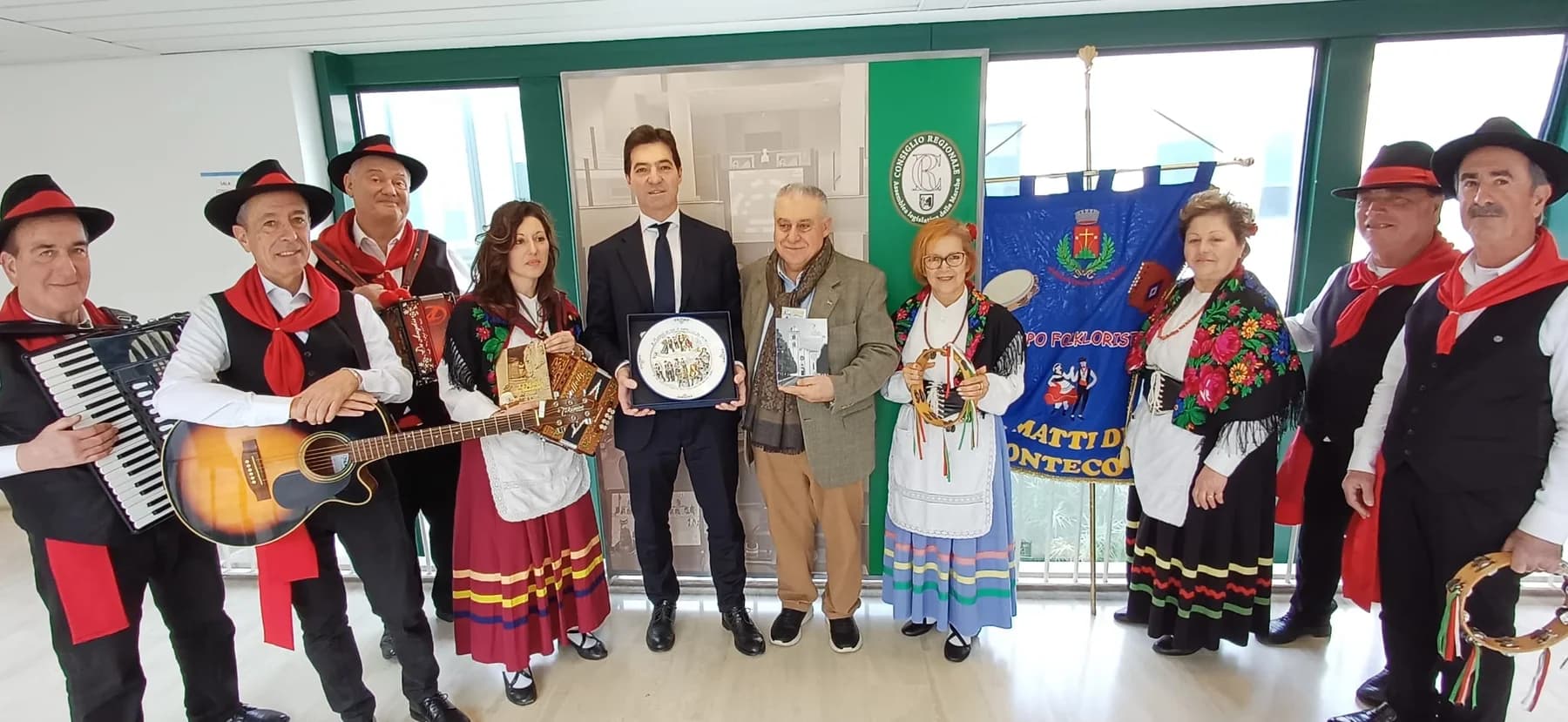 Il gruppo folkloristico in costume attorno al piatto incorniciato, davanti allo stendardo del gruppo e all'insegna del Consiglio Regionale delle Marche.