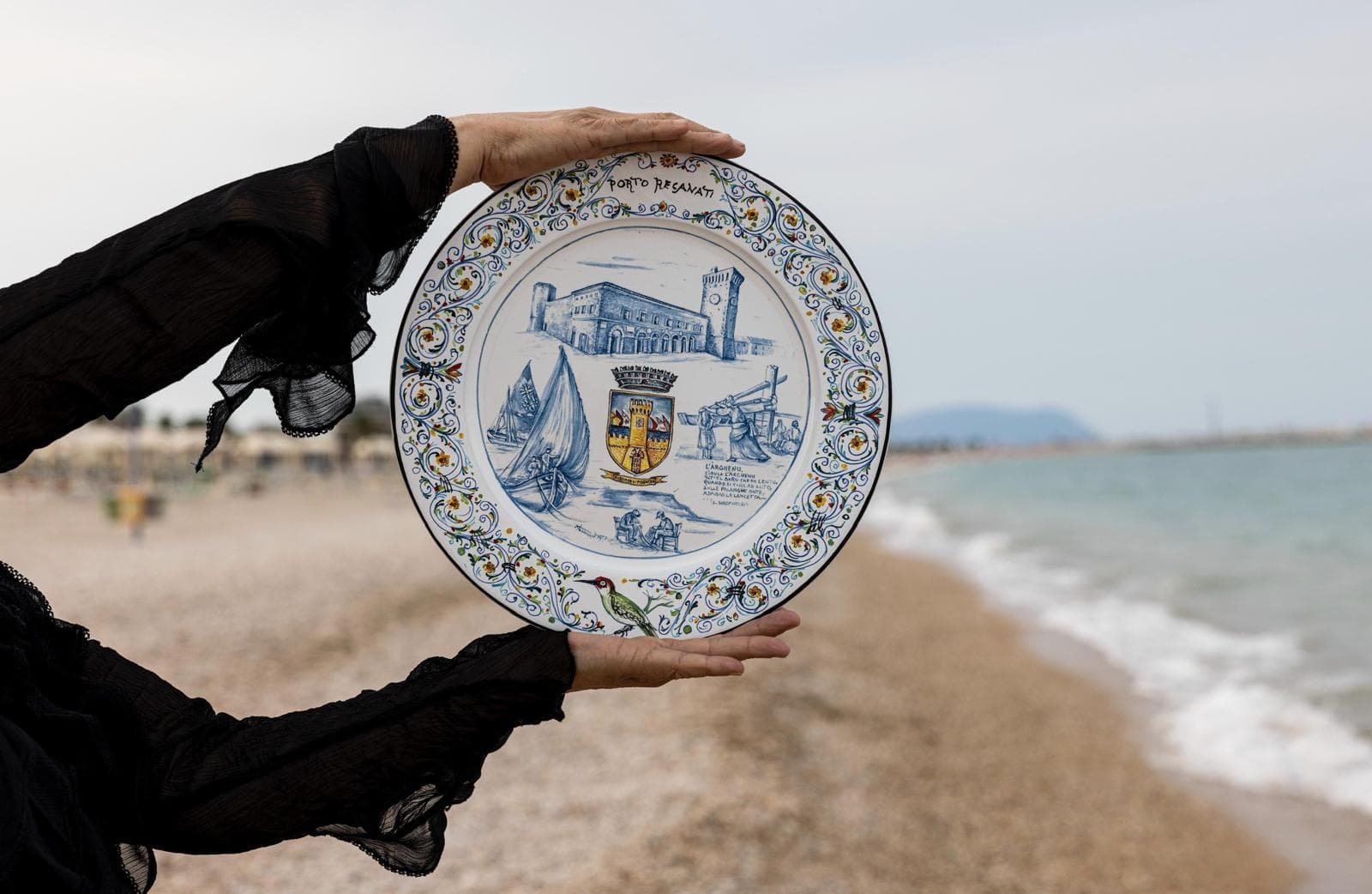 Paola Iannucci regge un piatto in maiolica davanti al mare, sulla battigia.