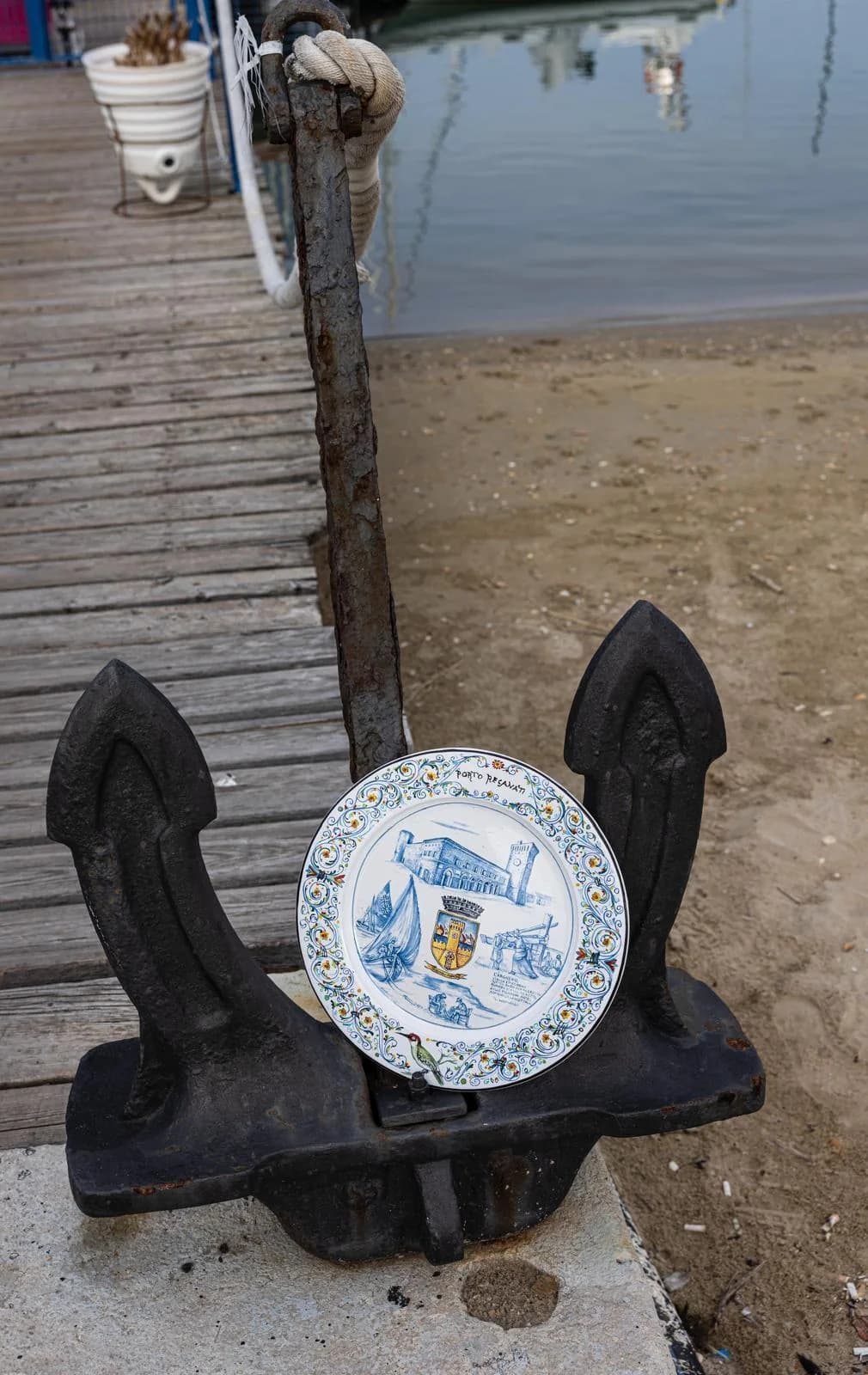 Un piatto in maiolica incastrato fra due sagome di ferro nero, sul pontile di legno.
