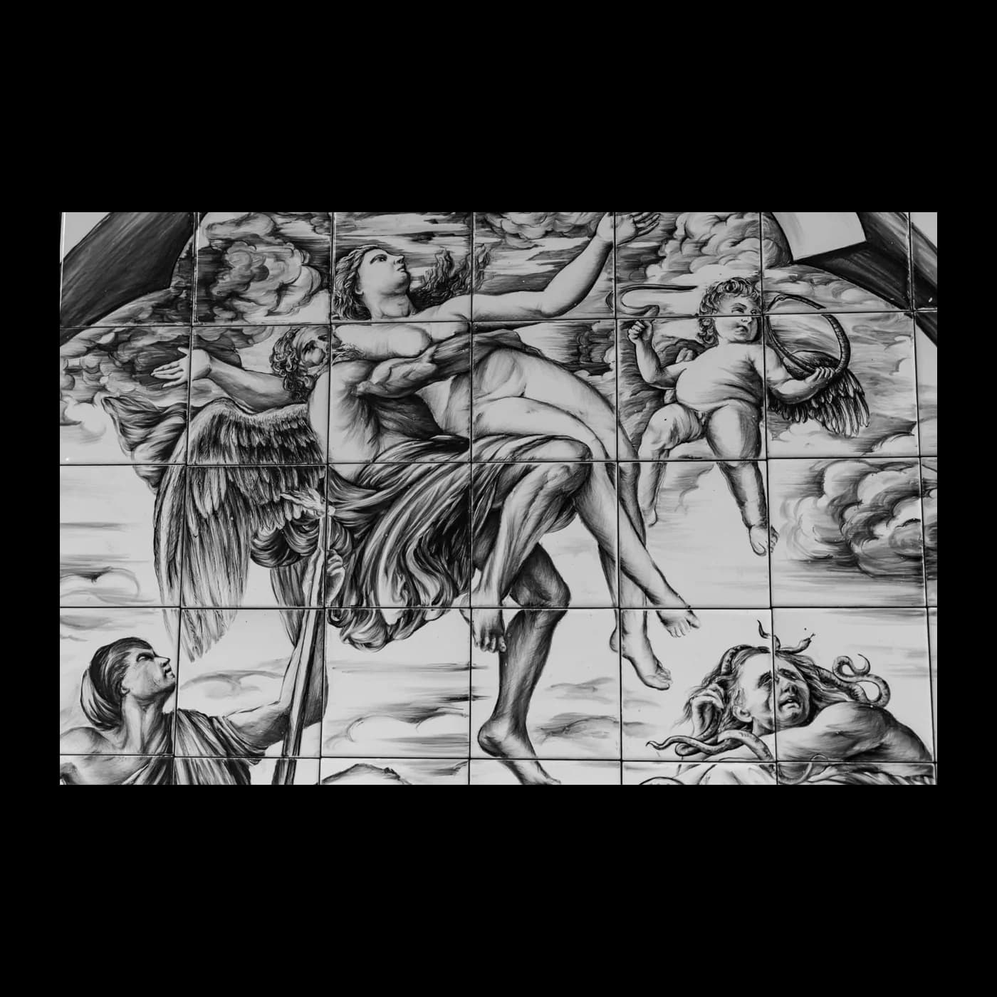 Pannello composto da molte piastrelle in ceramica, dipinto in monocromo con figure in volo e panneggi mossi.